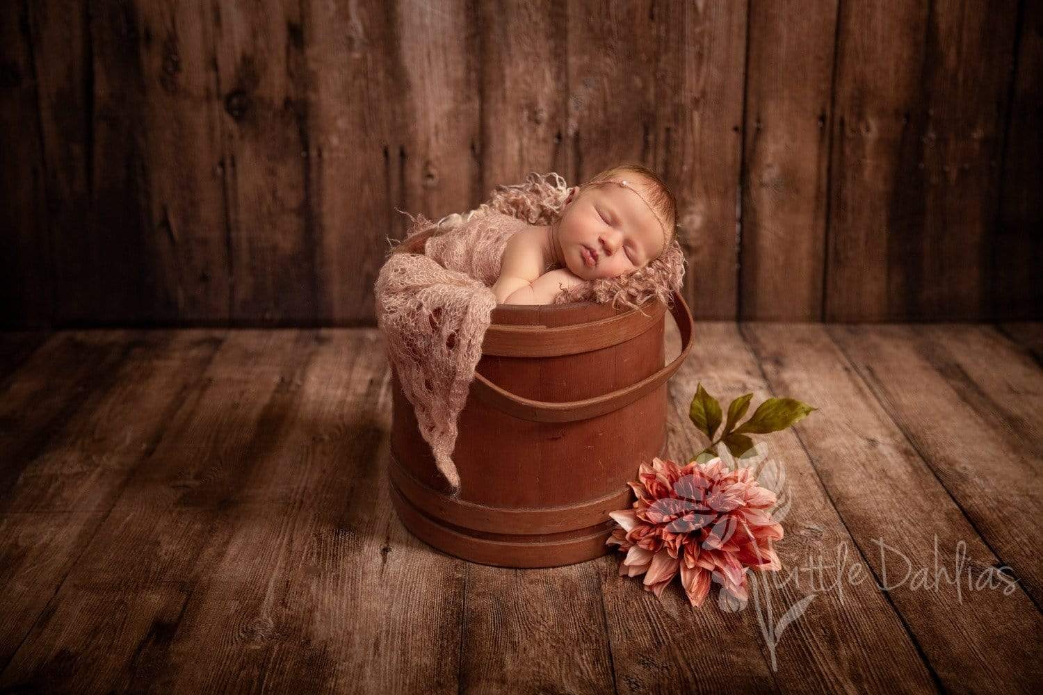 A newborn lying on the wooden prop in front of a wooden backdrop