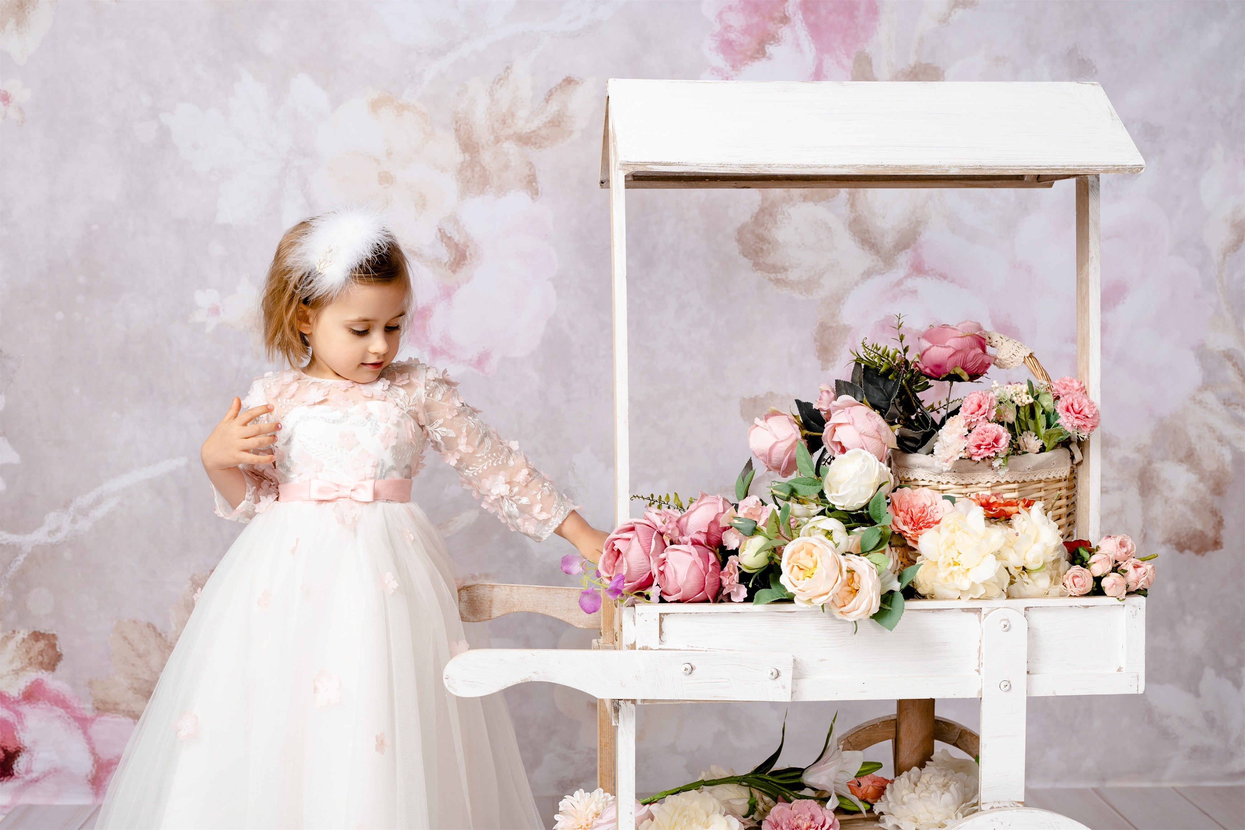 a little girl standing in front of a flower backdrop next to flower trolley