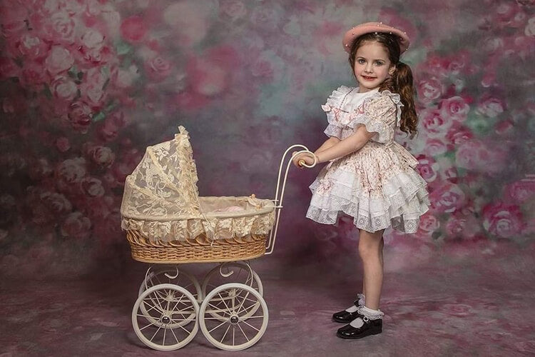 Little girl pushing a trolley standing in front of a flower sweep backdrop