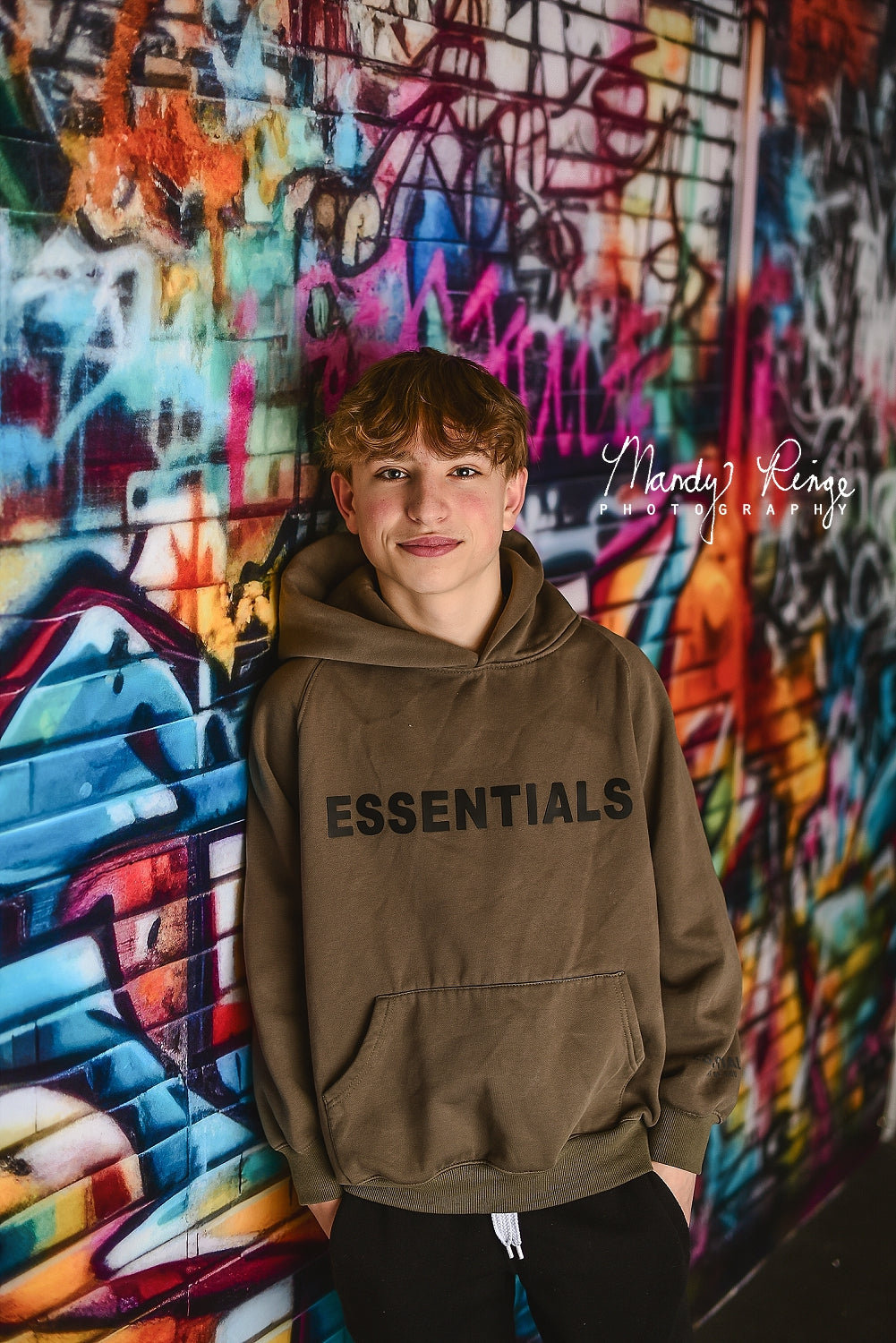 A boy standing besides graffiti wall backdrop