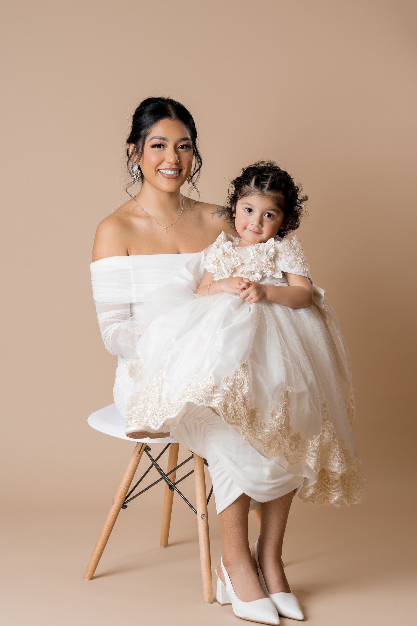 Mother-daughter in white dress sitting in fron of a beige paper backdrop