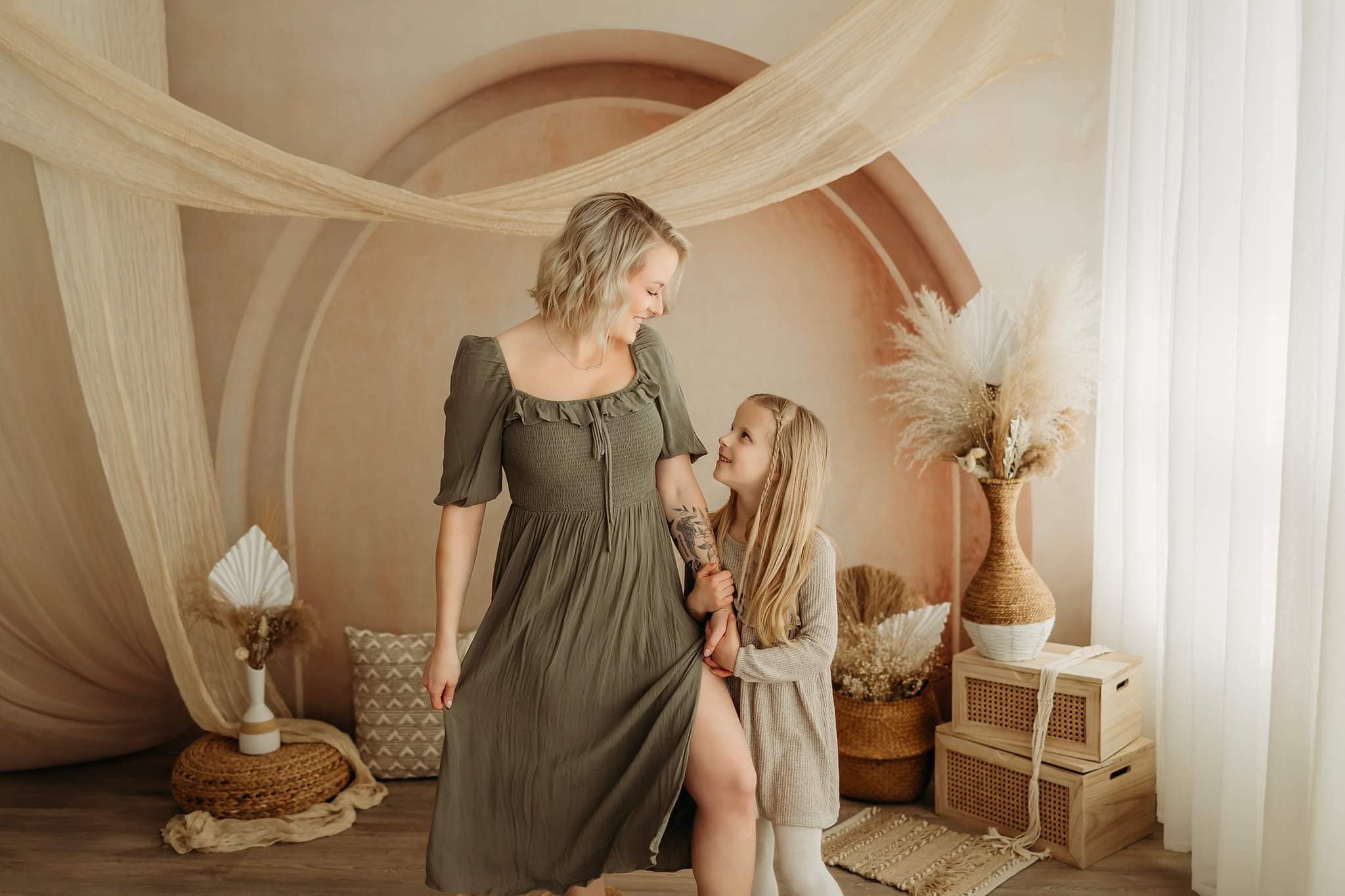 Mother and daugther standing and smiling at each other in front of a Boho screen backdrop