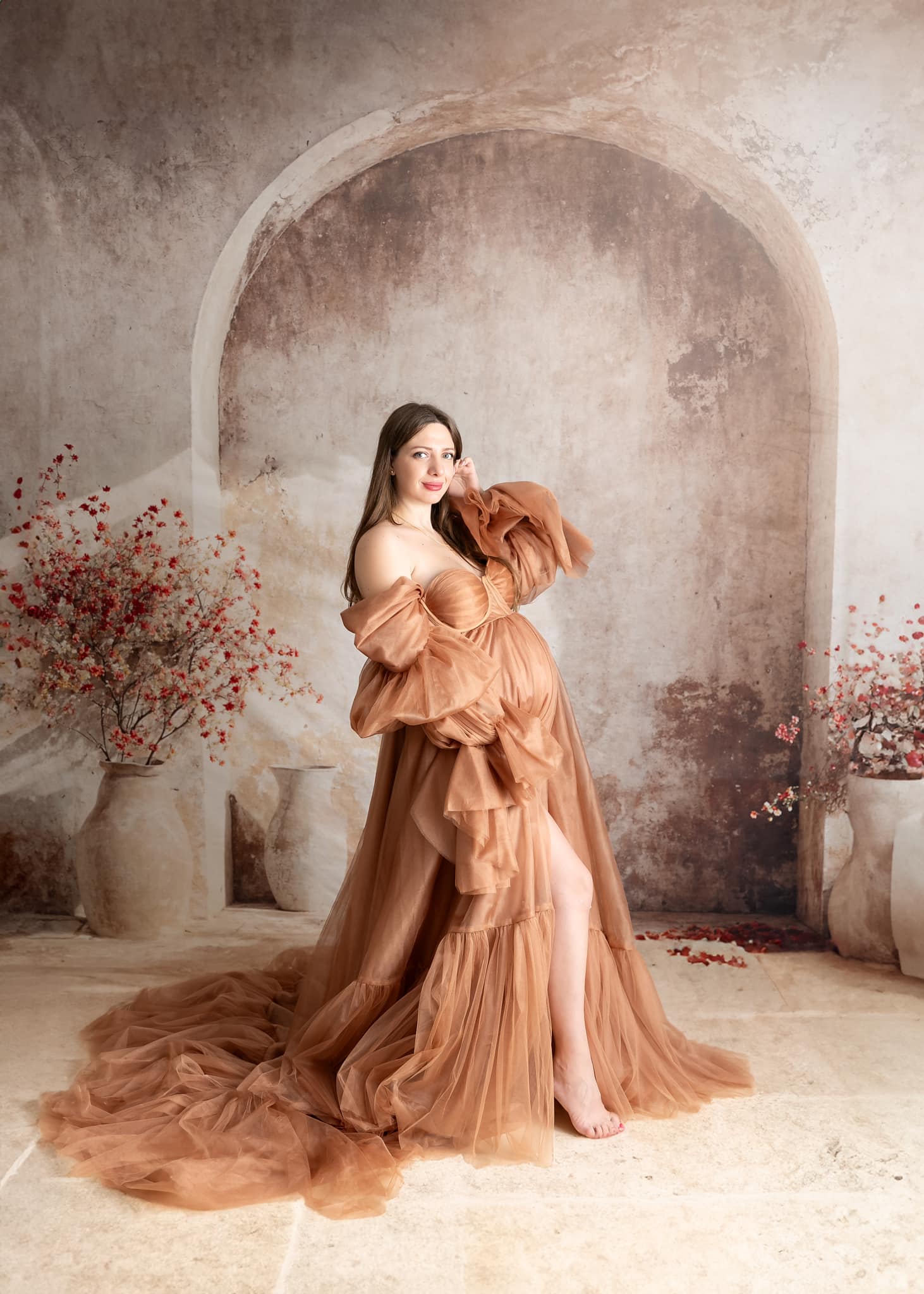 A pregnant woman with brown dress standing in front of a boho arch backdrop