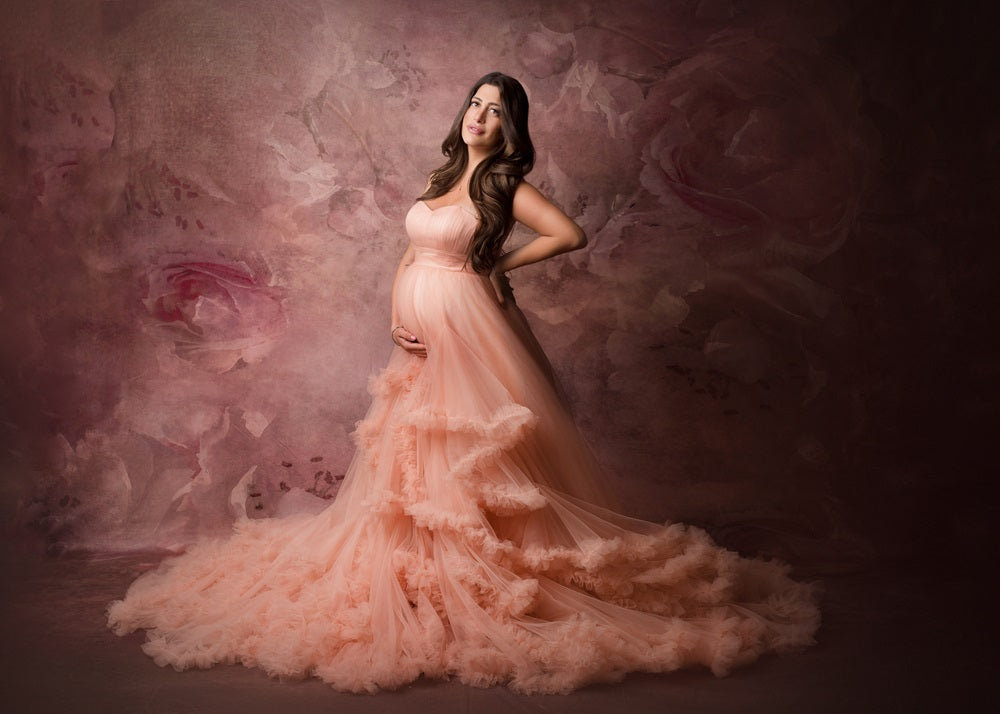 A pregnant woman standing in front of a fine art floral backdrop